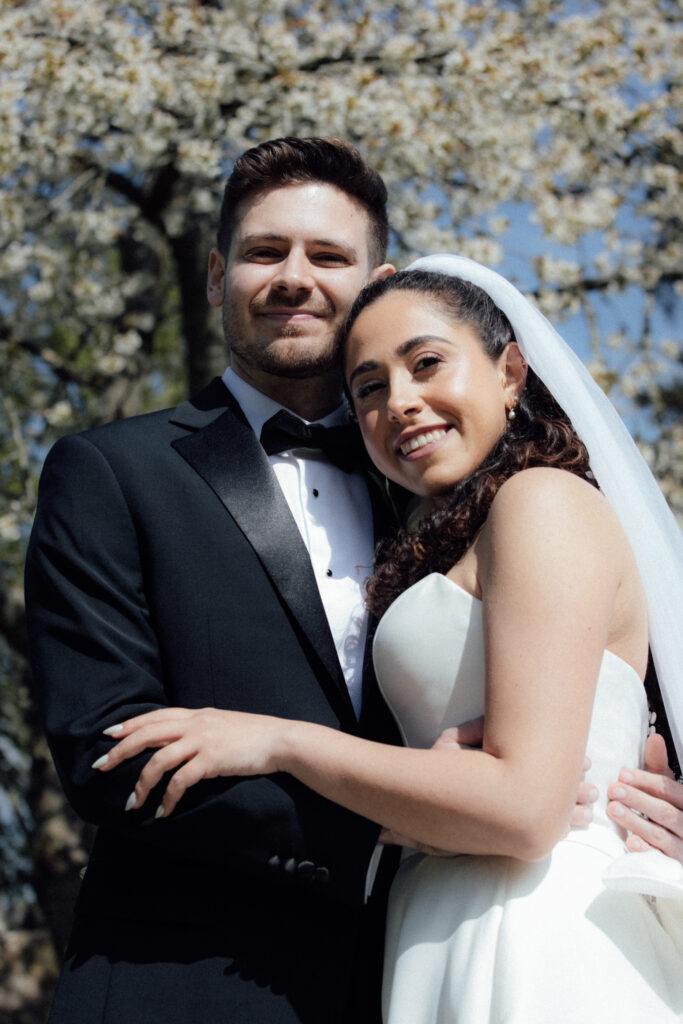 Bride and groom embracing and smiling outdoors beneath blooming trees at Borthwick Castle during a spring wedding portrait session.