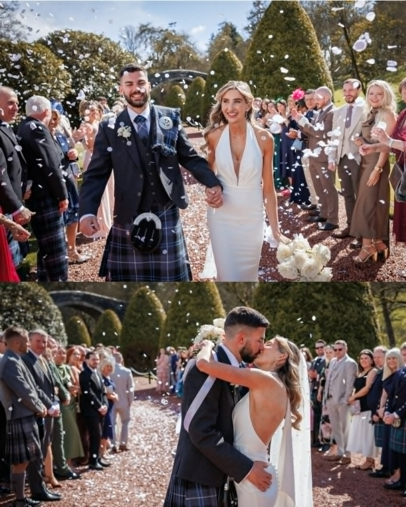 Bride and groom celebrating their wedding at Brig o’ Doon in Alloway, walking hand in hand through a confetti shower before sharing a kiss surrounded by guests, with the groom dressed in a traditional Scottish kilt and the bride in a sleek white gown holding a white rose bouquet.
