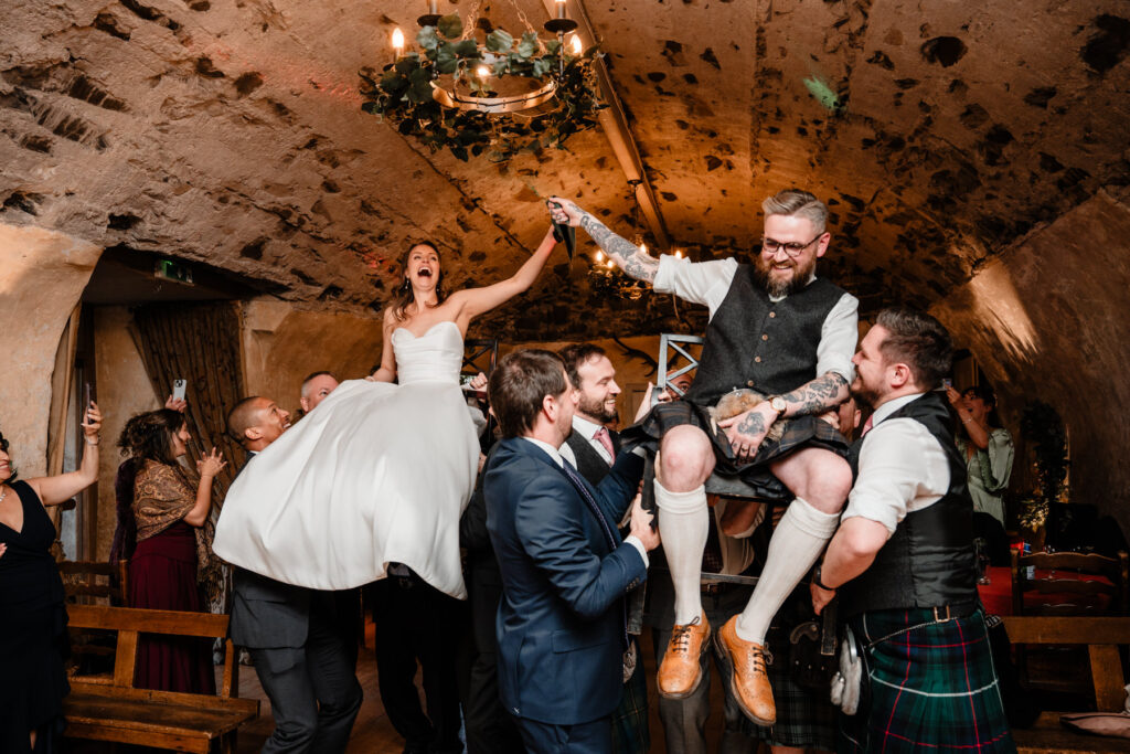 Bride and groom are lifted by friends during a lively Scottish castle wedding celebration