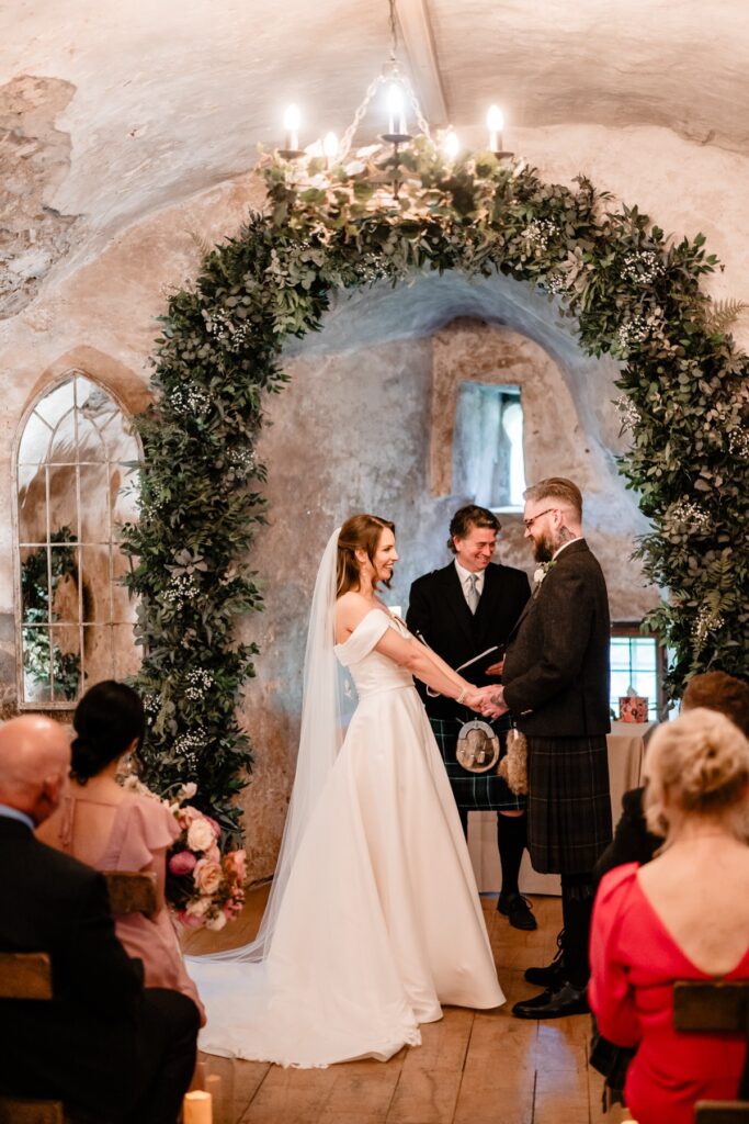 Bride and groom exchange vows beneath a lush floral arch at a Scottish castle wedding