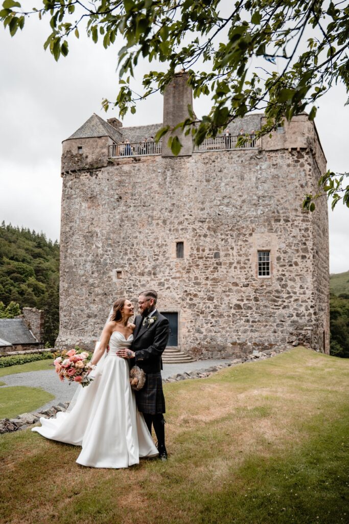 Bride and groom pose outside a historic Scottish castle during their wedding day
