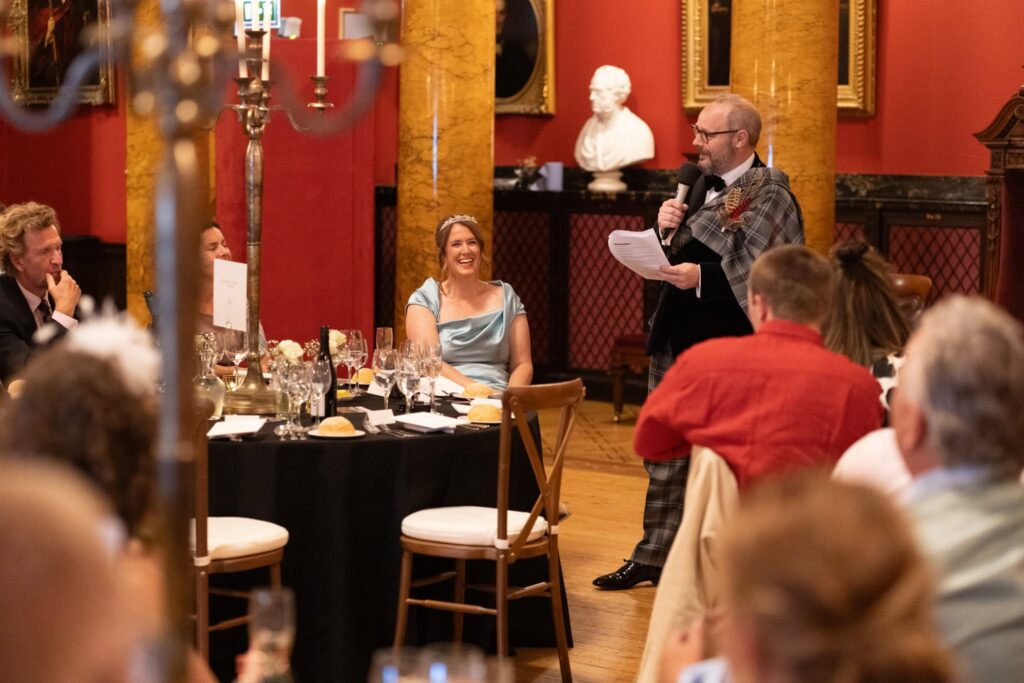 Groom delivers his heartfelt wedding speech during the reception at the Royal College of Physicians of Edinburgh as the bride smiles and guests enjoy the celebration.