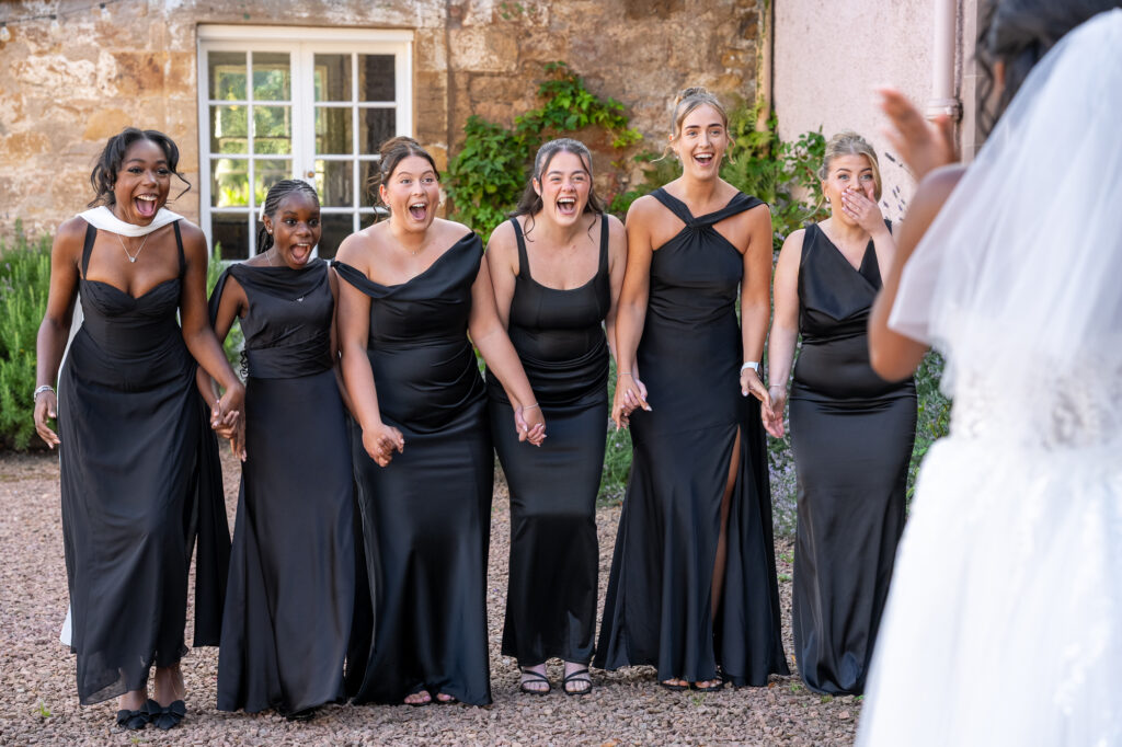 Bridesmaids reacting with surprise and excitement as they see the bride in her wedding dress for the first time during an emotional first look at Colstoun House.