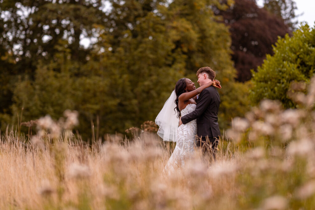 Bride and groom embracing in a wildflower meadow during their outdoor wedding portraits, sharing a joyful moment surrounded by tall grasses and lush greenery.